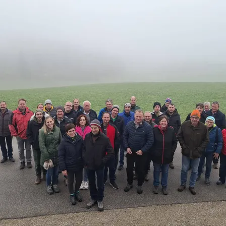 Eine Gruppe von Menschen in warmer Kleidung steht auf einer Straße und posiert für ein Foto mit einem nebligen Feld im Hintergrund.