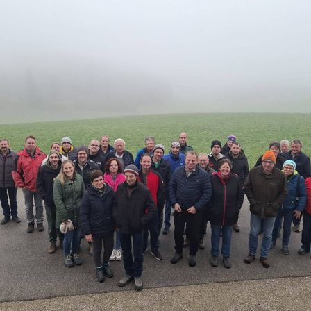 Eine Gruppe von Menschen in warmer Kleidung steht auf einer Straße und posiert für ein Foto mit einem nebligen Feld im Hintergrund.