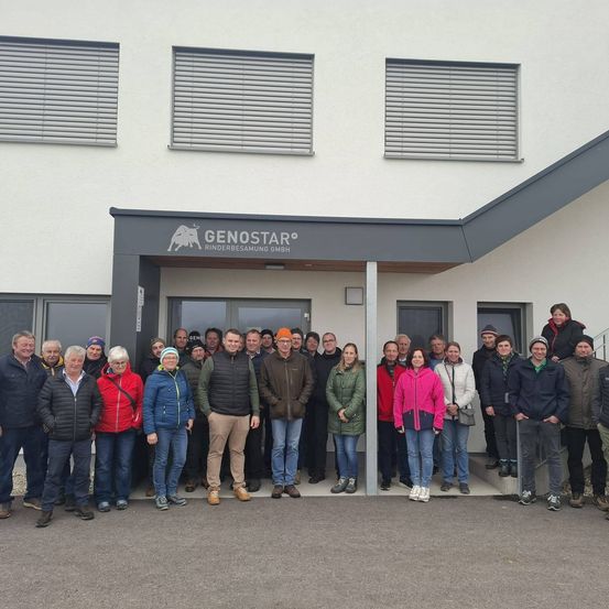 Eine Gruppe von Menschen in Winterkleidung steht vor einem Gebäude mit einem Schild, auf dem 'Genostar' steht.