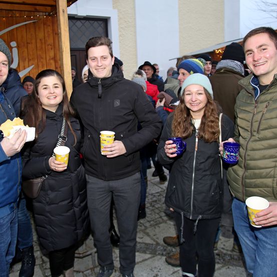 Eine Gruppe von Menschen steht draußen und lächelt. Drei Frauen und zwei Männer halten Tassen, einer der Männer hält Essen. Sie sind warm gekleidet für kaltes Wetter.