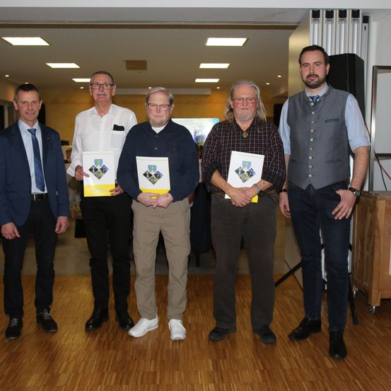Fünf Männer stehen auf einem Holzboden und halten Urkunden in der Hand. Sie scheinen für ein Foto zu posieren.