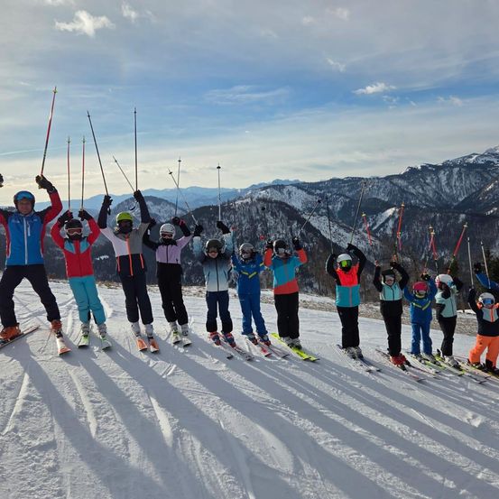 Eine Gruppe von Skifahrern posiert für ein Foto auf einem verschneiten Berg unter blauem Himmel. Sie tragen alle Skiausrüstung und halten Skistöcke.