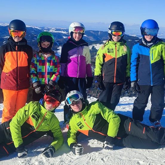 Eine Gruppe von Menschen ist auf einem verschneiten Berg. Sie tragen Skiausrüstung und Helme. Sie posieren für ein Foto.