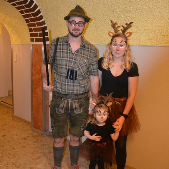 Eine Familie in Kostümen, mit einem Mann in einem Hirschkostüm, einer Frau in einem Rentierkostüm und einem Kind in einem schwarzen Kleid, posiert für ein Foto.