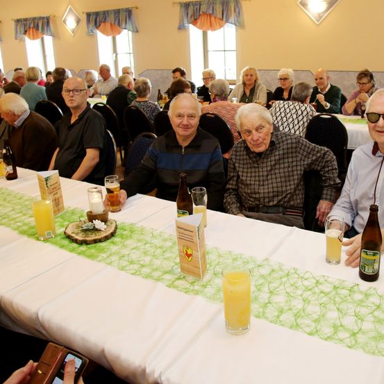 Eine Gruppe älterer Menschen sitzt in einem Restaurant an Tischen, einige mit Brille, lächelnd und genießt Getränke.