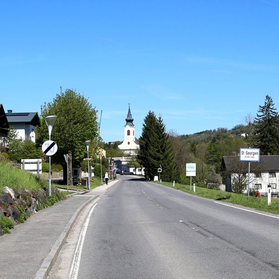 Eine breite Straße mit einer Kirche in der Ferne. Eine Person geht auf dem Bürgersteig. Die Straße ist leer ohne Autos.