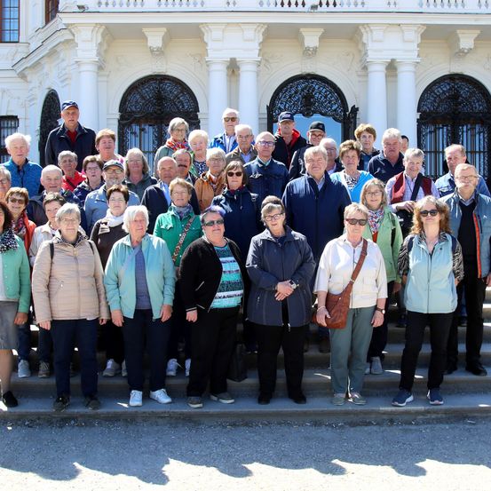 Eine große Gruppe von Menschen in lässiger Winterkleidung posiert für ein Foto vor einem prunkvollen Gebäude.