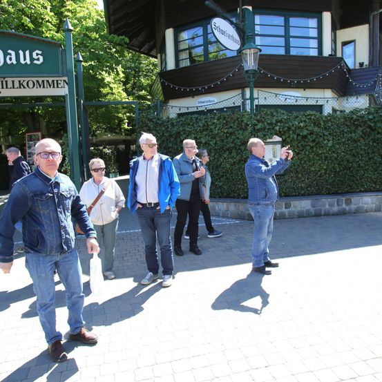 Eine Gruppe von Menschen geht vor einem Gebäude. Ein Mann macht ein Foto.