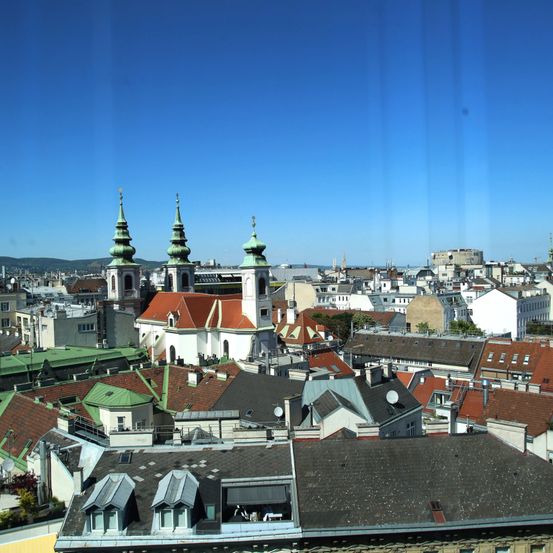 Luftaufnahme einer europäischen Stadt mit vielen Gebäuden, einige mit grünen Kuppeln, unter einem klaren blauen Himmel.