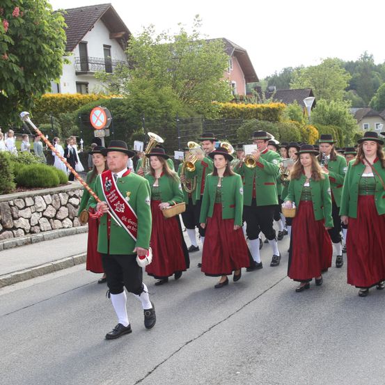 Eine Gruppe von Menschen in grünen und roten traditionellen Kostümen marschiert die Straße entlang und spielt Blech- und Holzblasinstrumente.