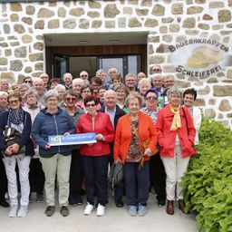 Eine Gruppe älterer Menschen posiert für ein Foto vor einem Gebäude mit einer Steinmauer. Das Gebäude hat ein Schild mit der Aufschrift "BAUENKRAPFEN SCHLEIFREI".