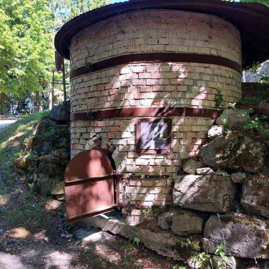 Ein Backsteinschornstein steht an einem Hang, umgeben von Felsen. Er hat einen offenen Bogeneingang und ein Schild an der Wand.