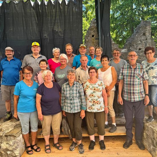 Eine Gruppe von Erwachsenen, hauptsächlich Senioren, posiert für ein Gruppenfoto vor einer Steinmauer und Grün.