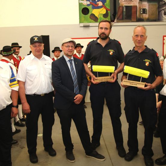 Drei Männer in Uniformen mit Trophäen stehen nebeneinander in einem Raum mit einem Wandgemälde.