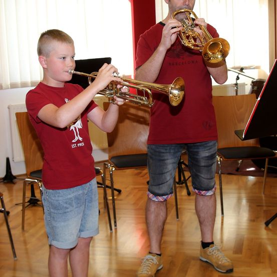 Ein junger Junge steht und spielt Trompete, während ein Mann neben ihm steht und ebenfalls Trompete spielt.
