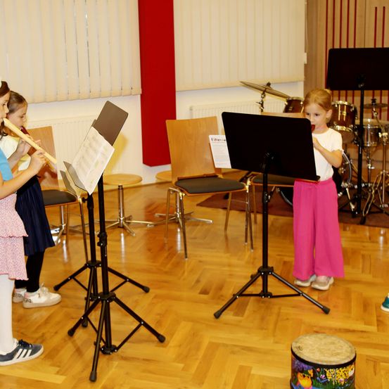 Zwei junge Mädchen üben ihre Musikinstrumente, eine spielt Flöte und die andere Schlagzeug, mit Notenständern vor ihnen.