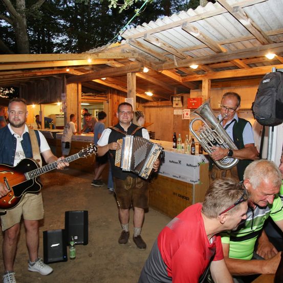Eine Gruppe von Musikern spielt in einem Zelt mit Holzwänden. Ein Mann spielt Gitarre, der andere Akkordeon.