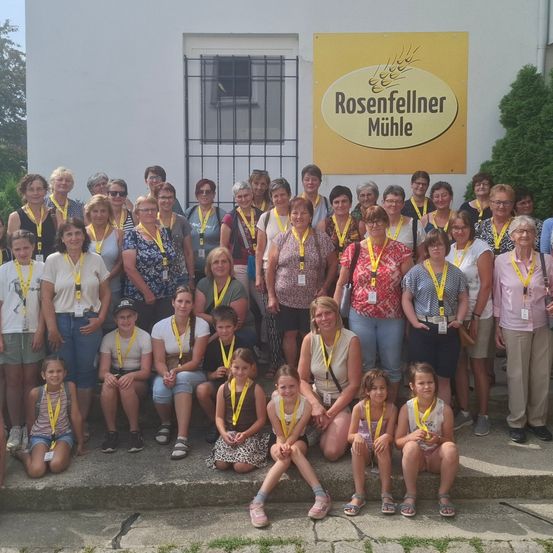 Eine Gruppe von Erwachsenen und Kindern mit gelben Namensschildern posiert für ein Foto vor dem Gebäude der Rosenfellner Mühle.