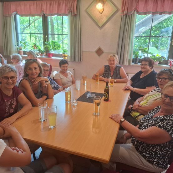 Eine Gruppe von Frauen sitzt um einen Tisch mit Biergläsern und Getränken und posiert lächelnd für ein Foto.