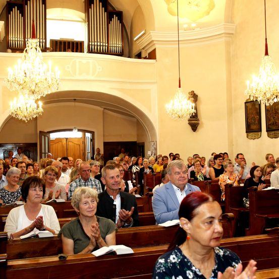 Eine Gemeinde in einer Kirche, die klatscht und lächelt, mit Kronleuchtern und einer Orgel im Hintergrund.
