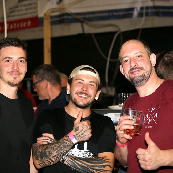 Drei Männer bei einem gesellschaftlichen Treffen, einer hält ein Bierglas, ein anderer gibt einen Daumen hoch und der dritte hat Tattoos an den Armen.