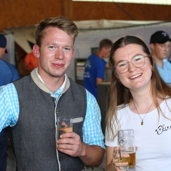 Ein Mann und eine Frau lächeln und halten Gläser mit Bier bei einer Veranstaltung im Freien.