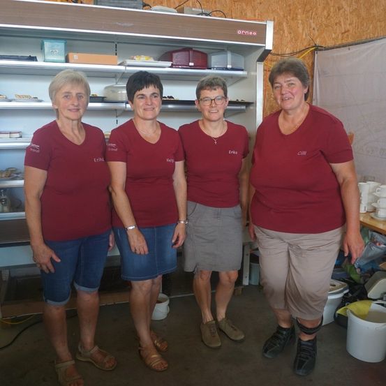 Vier Frauen in roten T-Shirts stehen in einem Raum mit einem Regal dahinter und lächeln für ein Foto.