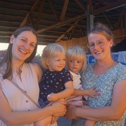 Drei Frauen und zwei kleine Kinder lächeln und posieren für ein Foto in einer Scheune. Die Frauen halten die Kinder.