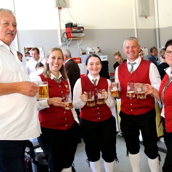 Fünf Personen in traditioneller deutscher Kleidung, lächelnd und Biergläser in der Hand in einem Raum.