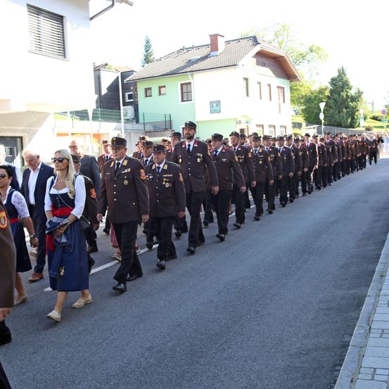 Eine Reihe von Militärangehörigen, die in Formation auf einer Straße marschieren, begleitet von Zivilisten in traditioneller Kleidung.