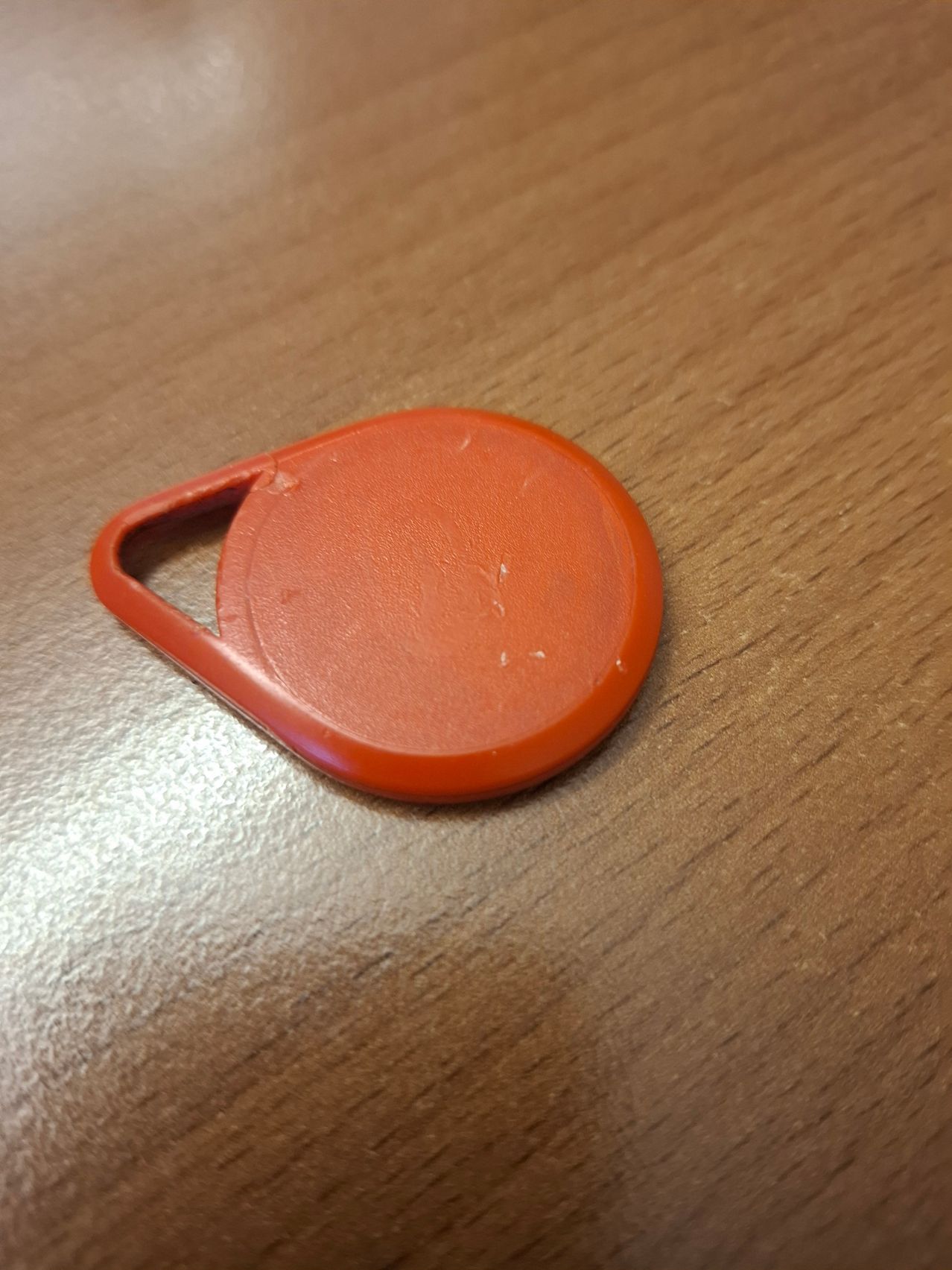 An orange plastic circular object with a keyring is placed on a wooden surface.