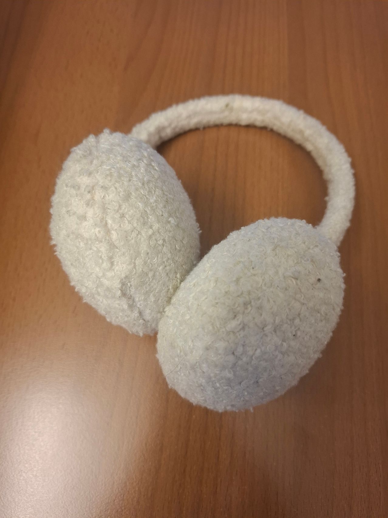 Ein Paar weißer pelziger Ohrenschützer liegt auf einer Holzoberfläche. Die Ohrenschützer haben eine weiche Textur und bedecken die Ohren vollständig.