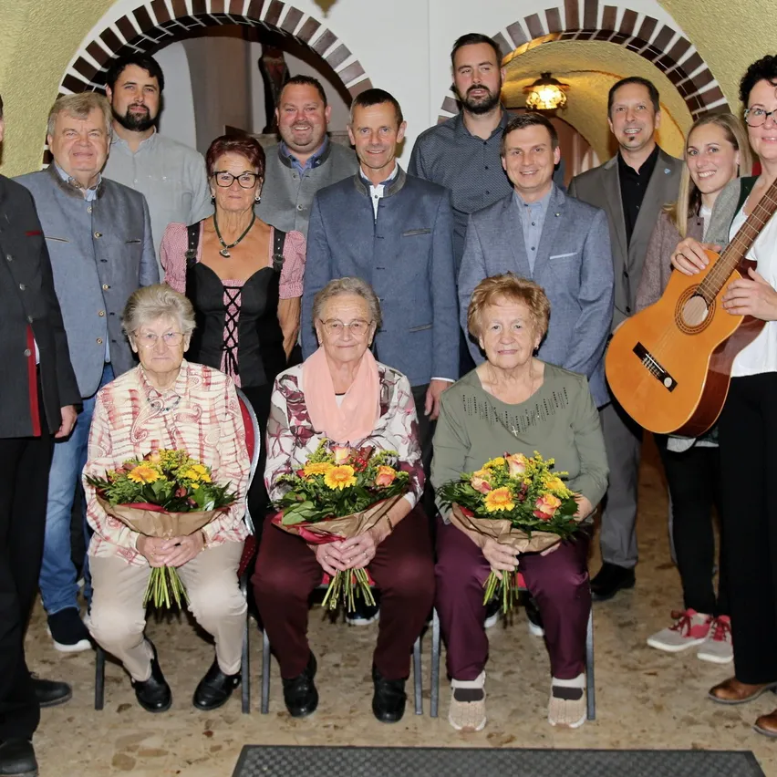 Gruppe mit Musikanten und Geehrten in Tracht und Anzügen mit Blumensträußen
