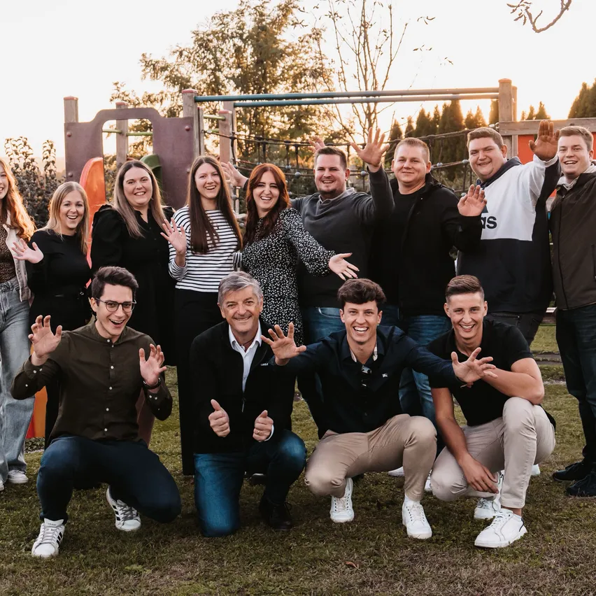 Eine Gruppe von Männern und Frauen posiert für ein Foto in einem Park mit Spielplatzgeräten im Hintergrund.