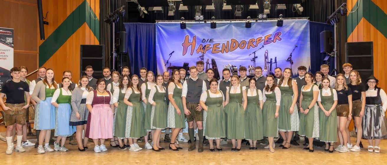Eine Gruppe von Menschen in traditioneller Kleidung posiert für ein Bild auf der Bühne mit Musikinstrumenten im Hintergrund.