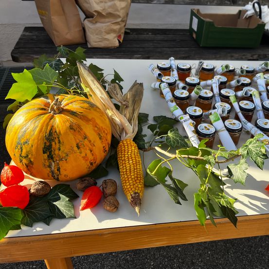Ein Tisch mit Herbstdekorationen, darunter eine Kürbis, Mais, Walnüsse und rote Papierlaternen. Viele Gläser mit Honig sind ordentlich auf dem Tisch angeordnet.
