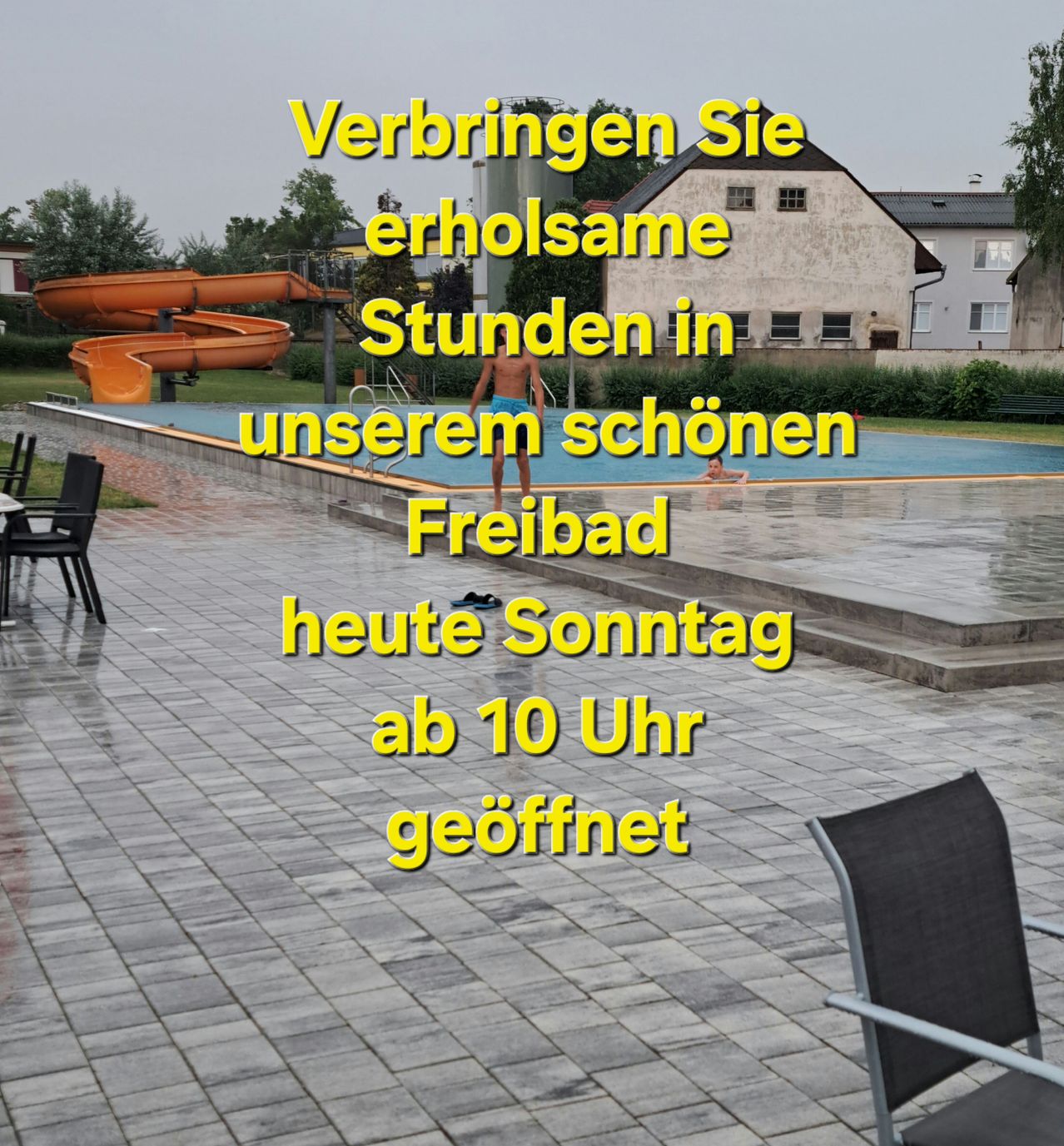 Ein Freibad mit einer einladenden Botschaft zum Genießen von erholsamen Stunden. Ein Mann steht in der Nähe des Beckens und ein anderer schwimmt. Stühle und Tische sind in der Nähe angeordnet. Im Hintergrund ist eine Wasserrutsche zu sehen.