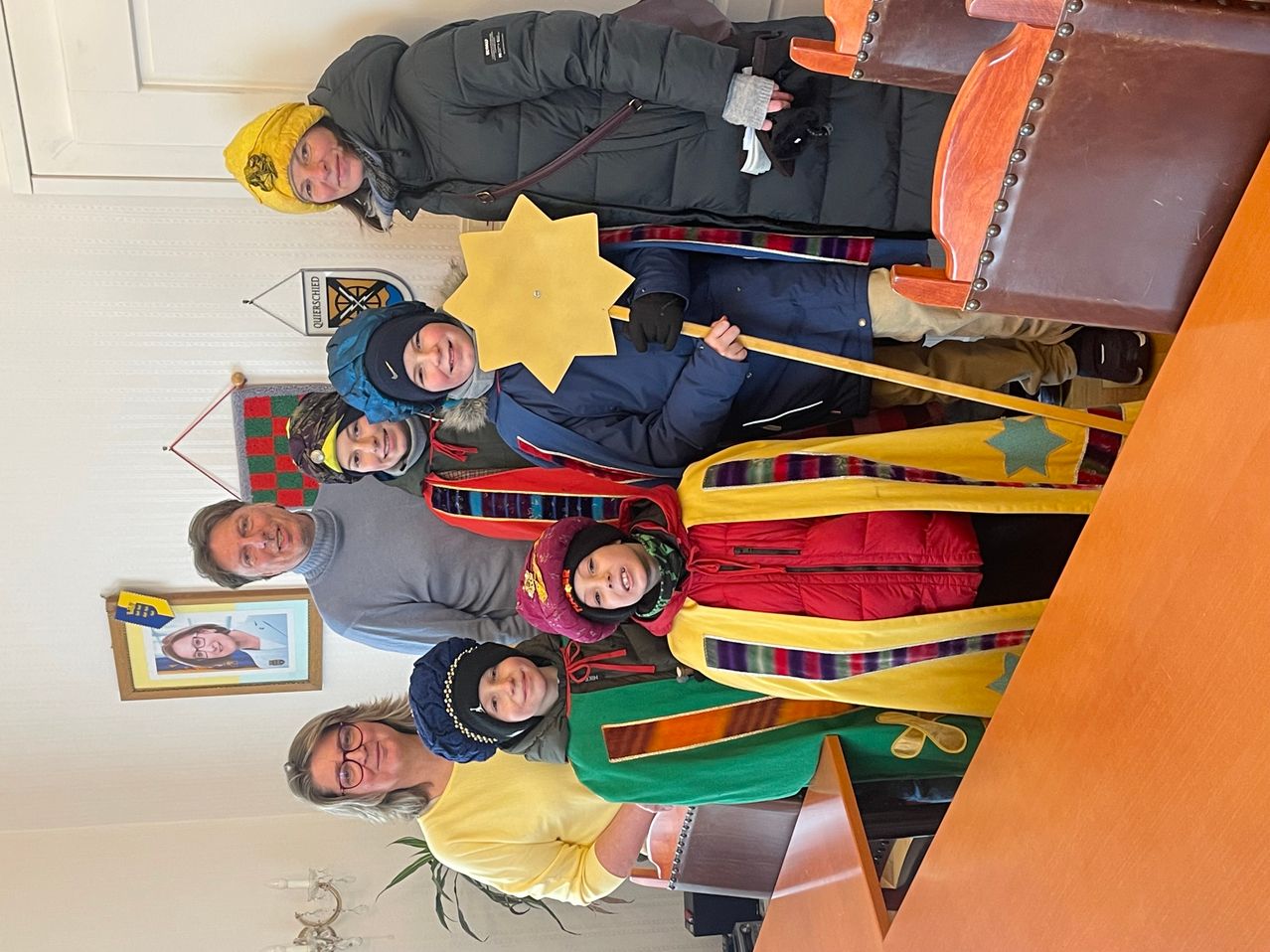 Eine Gruppe von Menschen in Winterkleidung, die lächelnd und mit einem Stern und einem Stab für ein Foto posieren. Ein Mann und eine Frau sind vorne.