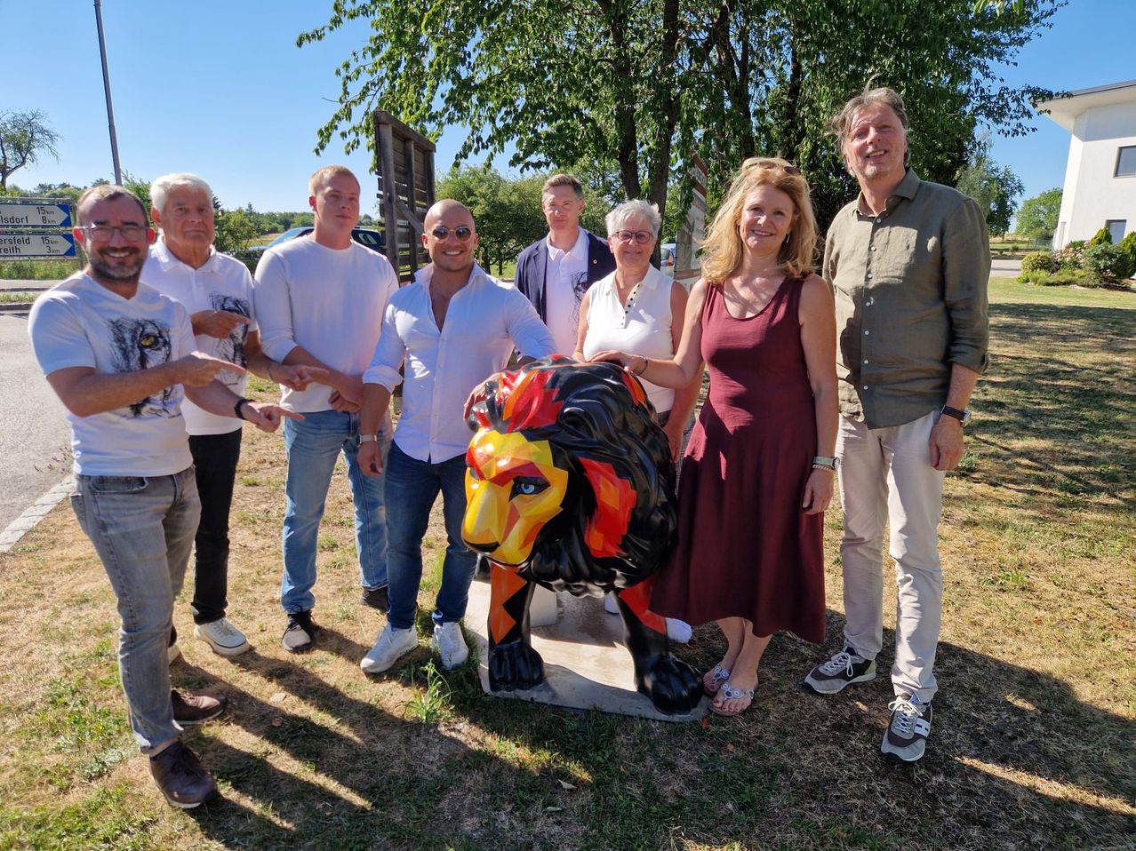 A group of people are standing around a large lion statue in a park. The statue is brightly colored and the people are smiling.