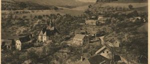 Ein Luftbild einer kleinen Stadt mit vielen Häusern, Bäumen und einem Gebirgszug im Hintergrund.