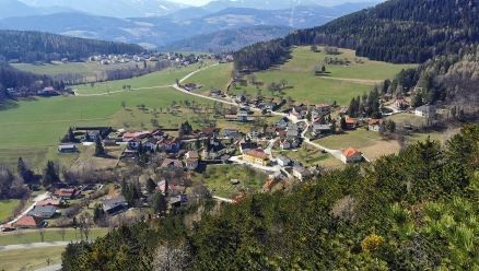 Ein Dorf liegt eingebettet in einem grünen Tal, umgeben von Bergen und Bäumen. Häuser sind über das Gebiet verstreut.