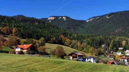 Ein landschaftlicher Blick auf eine ländliche Umgebung mit einem grünen Feld, einem Haus und Bergen im Hintergrund.