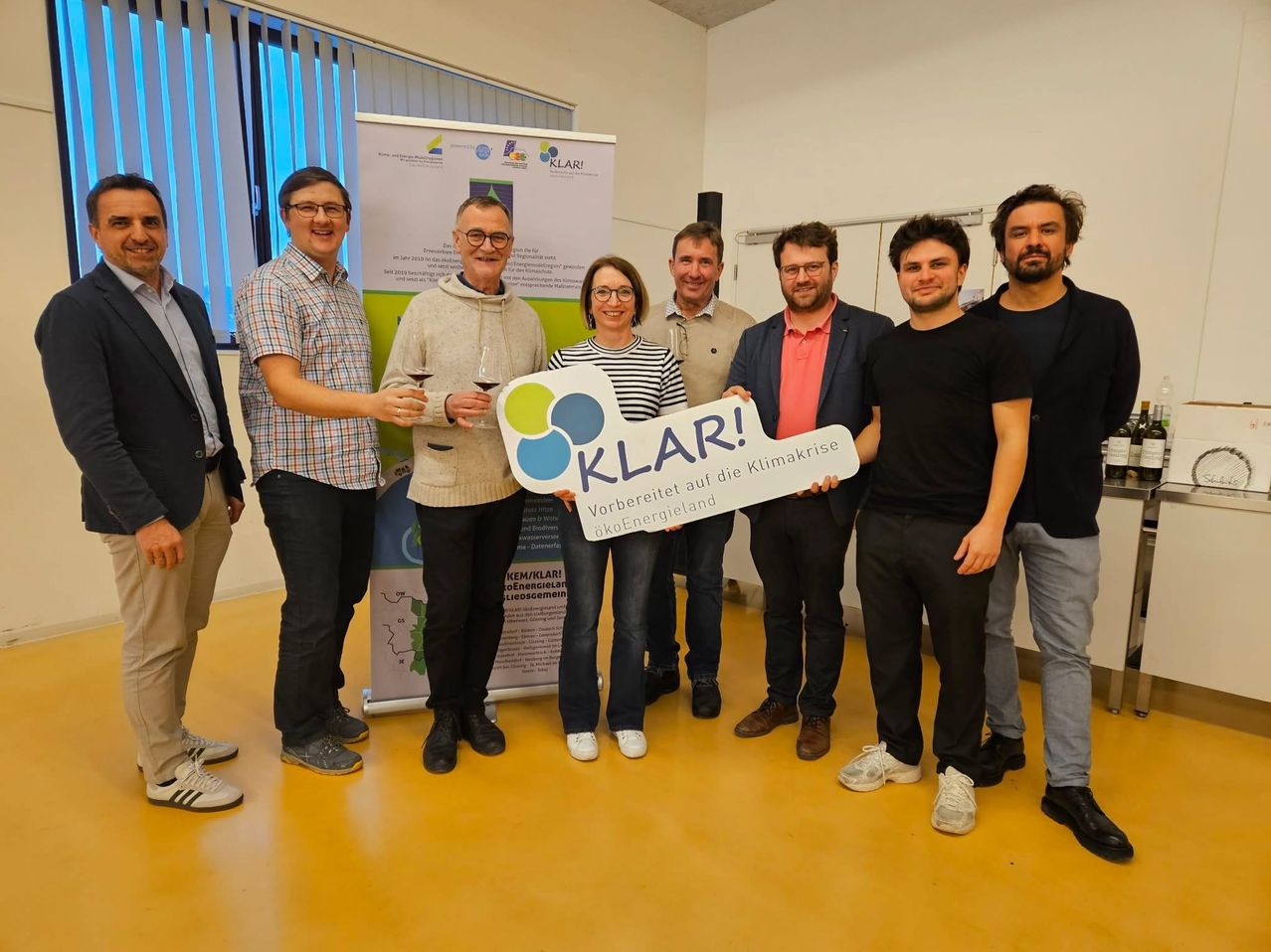 A group of people stand in a room holding a sign that says 'KLAR!' They are smiling and appear to be at an event.