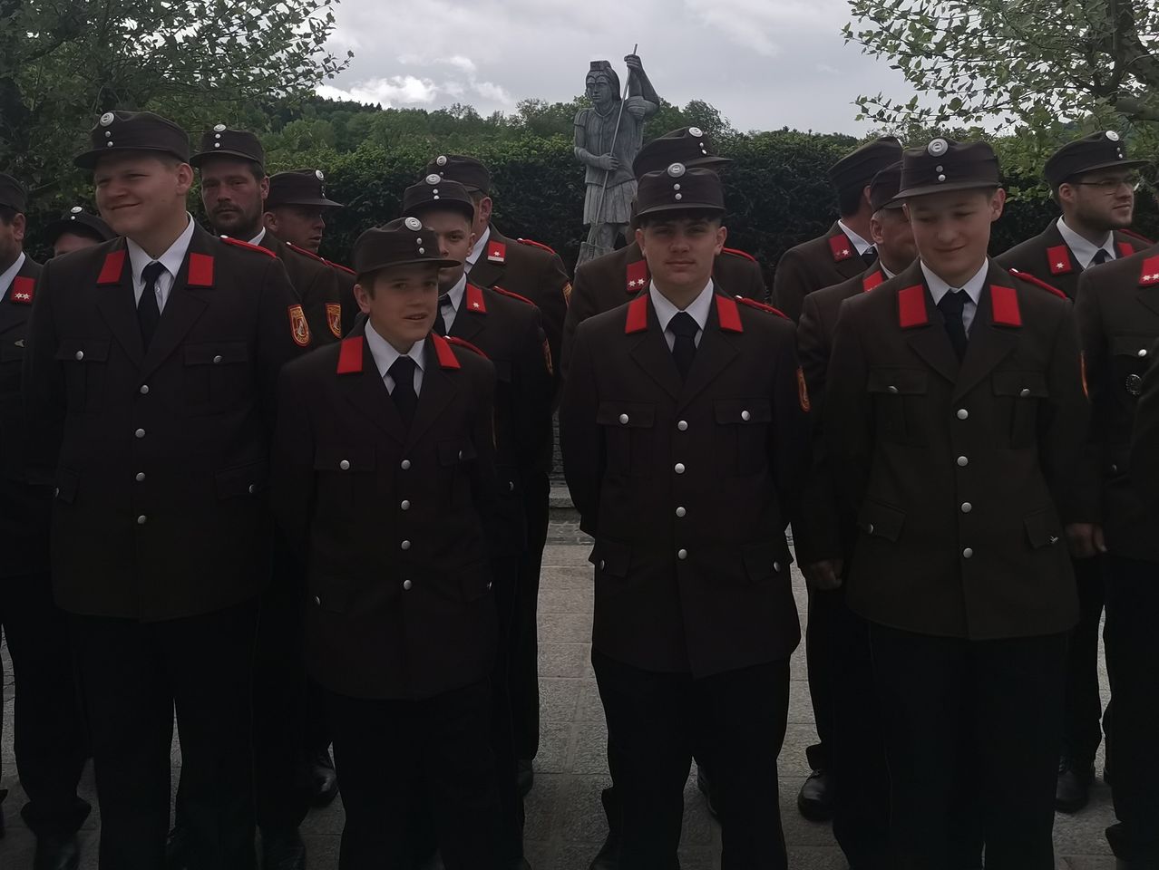 Eine Gruppe junger Männer in Militäruniformen steht an einem bewölkten Tag vor einer Statue.