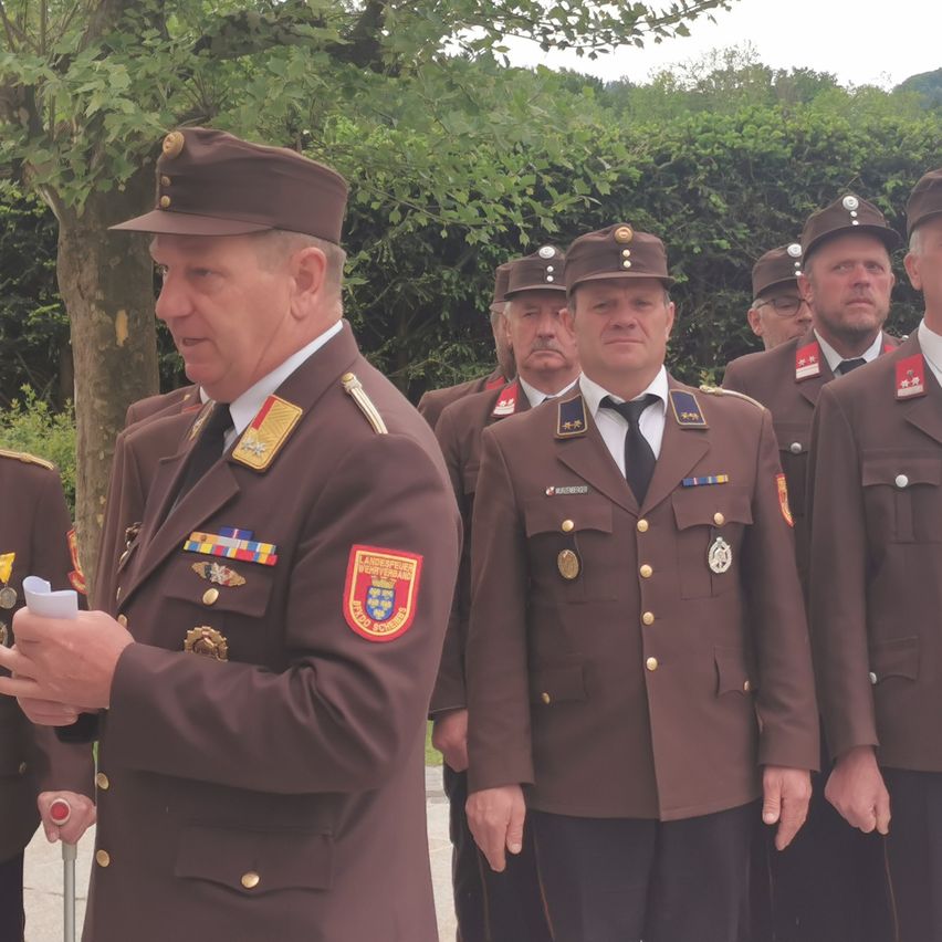 Eine Gruppe von Männern in Militäruniformen steht im Freien vor Bäumen und Grünpflanzen. Die Männer tragen Mützen und haben Abzeichen und Medaillen an ihren Uniformen.