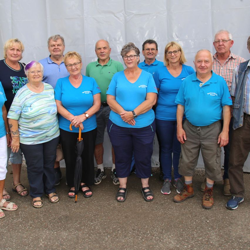Eine Gruppe von Erwachsenen, überwiegend Frauen, posiert für ein Foto. Sie tragen lässige Sommerkleidung, und einige haben Brillen. Ein weißer Zelt steht hinter ihnen.