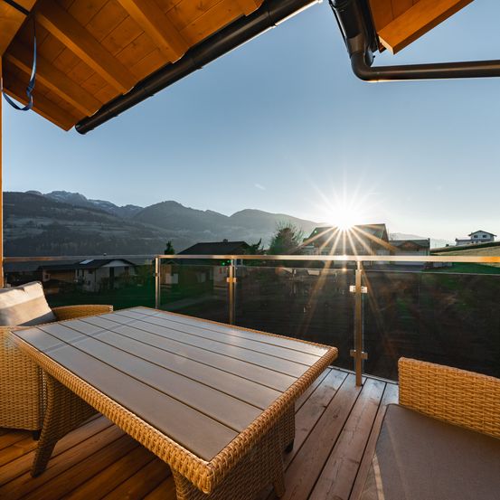 Ein Balkonblick mit Holzmöbeln und einem atemberaubenden Sonnenuntergang über den Bergen.