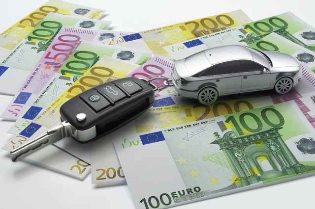 Ein Autoschlüssel liegt auf einem Stapel Euro-Banknoten. Der Schlüssel ist mit einem Spielzeugauto verbunden.