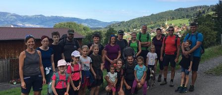 Eine Gruppe von Menschen, einschließlich Erwachsener und Kinder, steht auf der Straße und posiert für ein Foto, während einige Brillen, Hüte und Turnschuhe tragen.