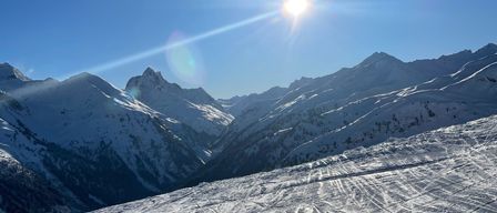 Die Sonne scheint hell über einer verschneiten Bergkette mit Skispuren auf den Hängen.